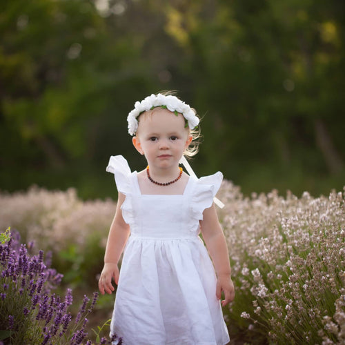 Small light haired child wearing a white rose flower crown and a white linen dress with ruffled sleeves. She's standing in the afternoon summer sun in a field of lavender. 