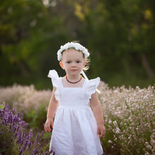 Load image into Gallery viewer, Small light haired child wearing a white rose flower crown and a white linen dress with ruffled sleeves. She&#39;s standing in the afternoon summer sun in a field of lavender. 