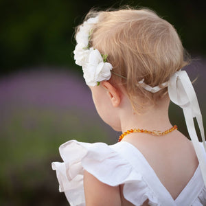Small light haired child wearing a white rose flower crown, tied with ribbon, and a white linen dress with ruffled sleeves. She's standing in the afternoon summer sun in a field of lavender.