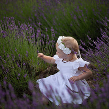 Load image into Gallery viewer, A small fair haired child wearing a white flower crown and white linen dress with ruffle sleeves sits in a field of lavender. She&#39;s picking a flower.